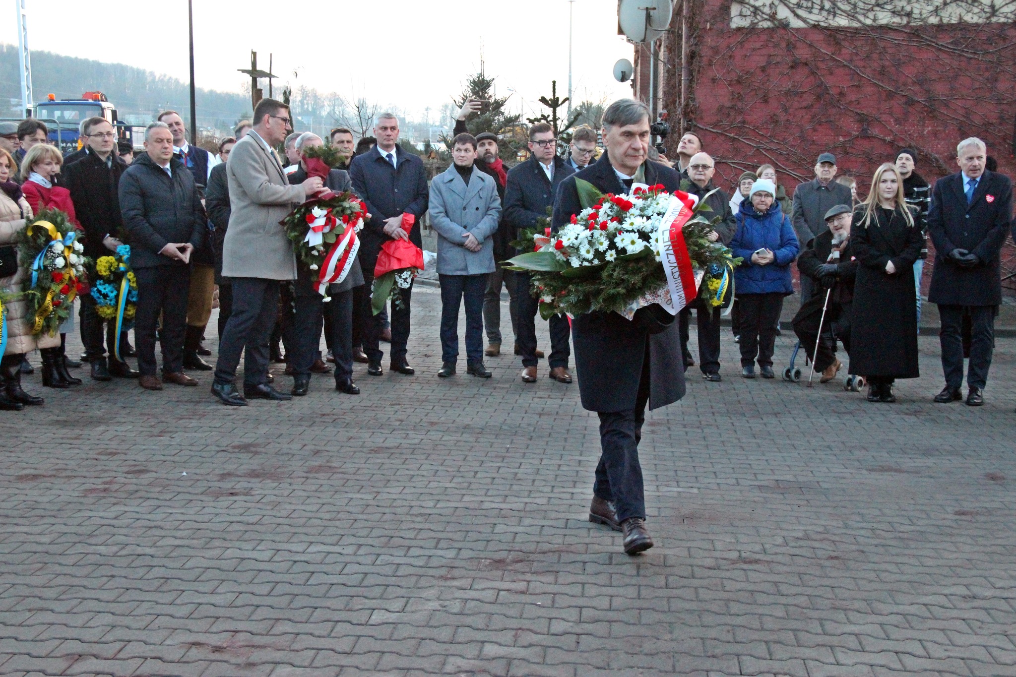 Uczestnik wydarzenia idzie z wieńcem do tablicy pamiątkowej