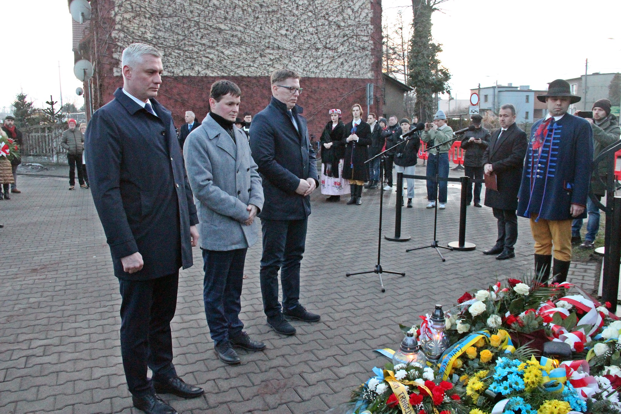 Trzech panów składa hołd przed tablicą pamiątkową
