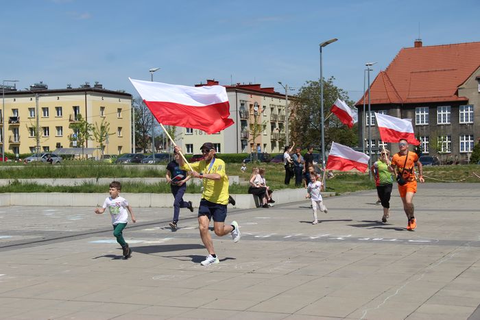 Ludzie i dzieci odbywają bieg z biało-czerwonymi flagami Polski.